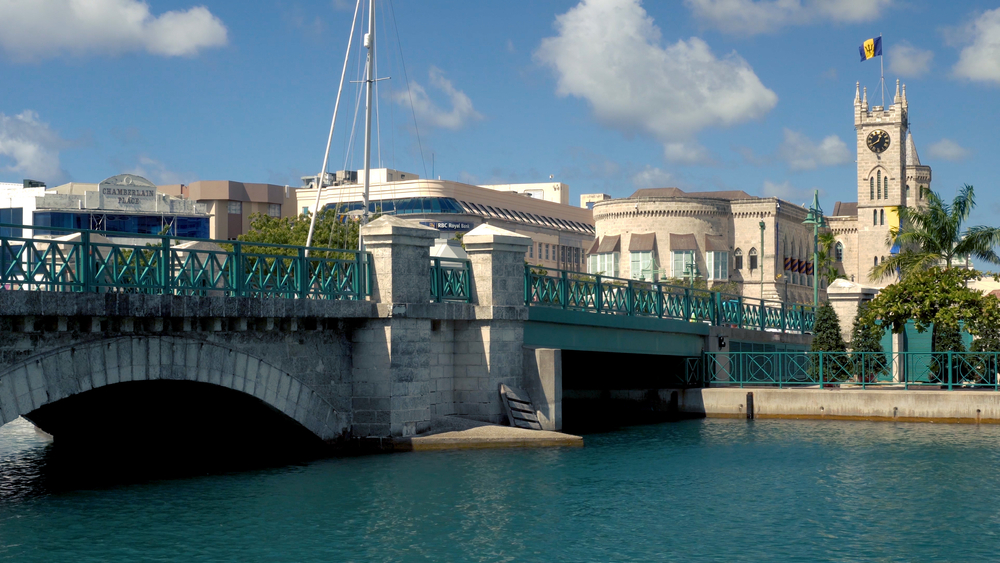Chamberlain bridge with people passing and Parliament building with the flag