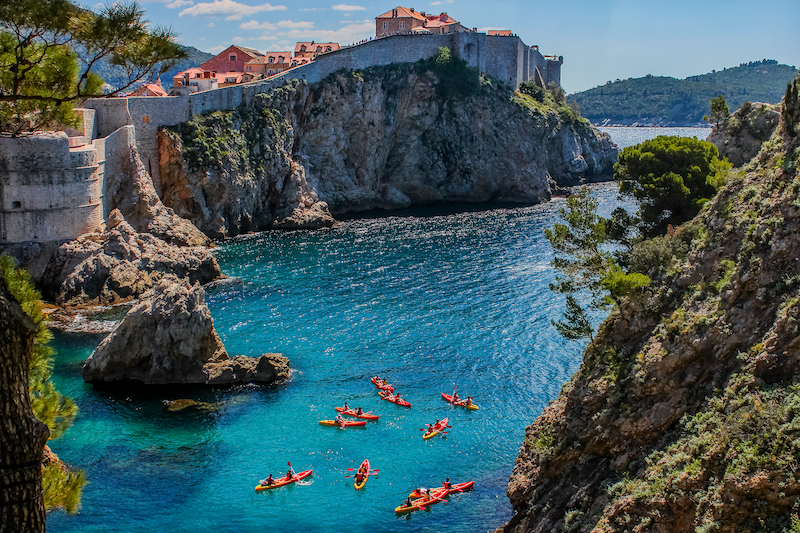 Dubrovnik city walls and old town colorful panorama on a summer day with sea kayaks in the foreground, Dubrovnik, Croatia.