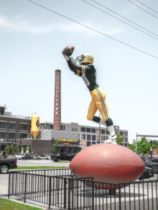 A larger than life 22 foot tall statue of Donald Driver extends his arm upward to catch a pass in front of the famous Titletown Brewery in Green Bay Wisconsin.