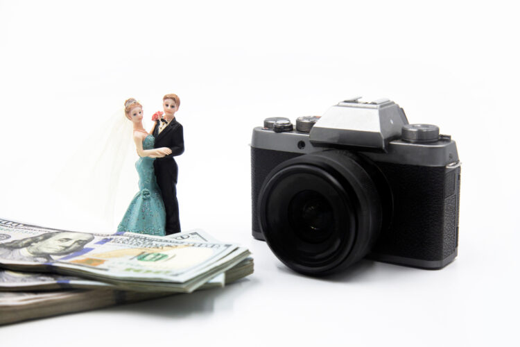 Wedding cake ornament of bride and groom next to a stack of bills and a camera