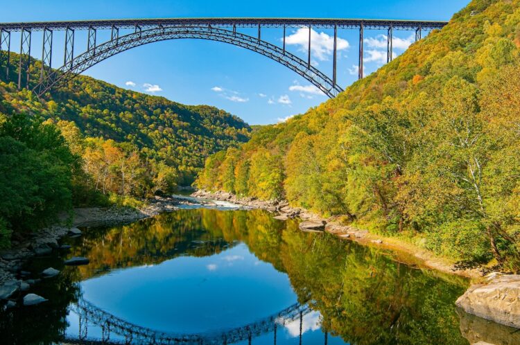 New River Gorge Bridge scenic view in fall. View from the lower gorge with reflection of the bridge in the river and fall foliage on the mountain sides. Horizontal color photo.