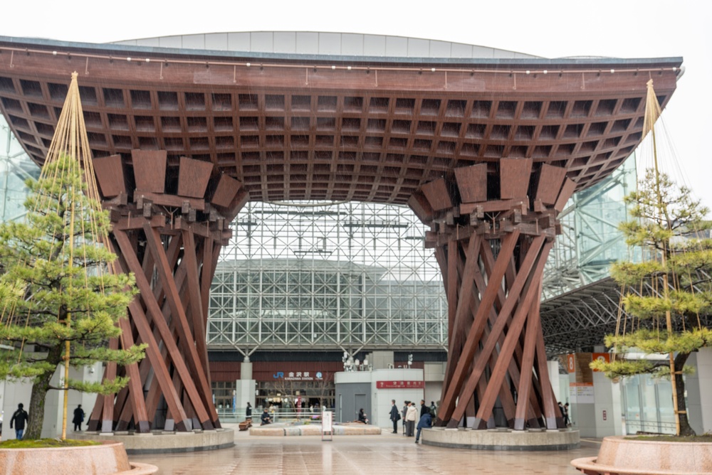 Kanazawa Station in Kanazawa, Japan, featuring the striking Tsuzumimon wooden gate inspired by traditional Japanese tsuzumi drums, modern glass dome roof, and bustling entrance plaza. A perfect blend of contemporary architecture and cultural heritage, this major transportation hub on the Hokuriku Shinkansen line is a popular landmark and tourist attraction in Ishikawa Prefecture