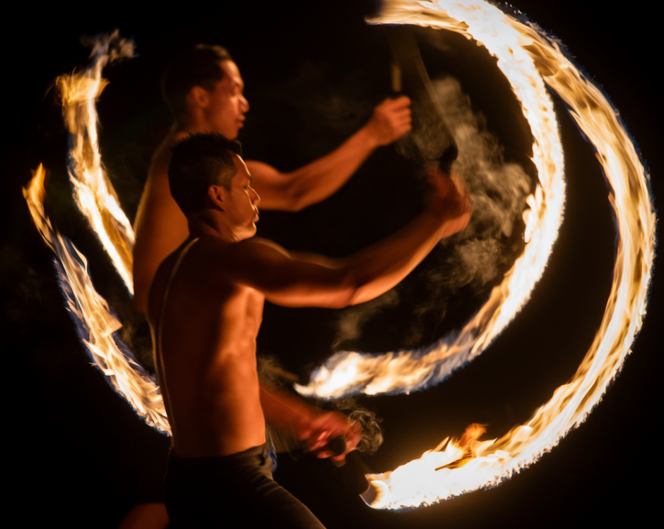 Two male Ahi Lele fire dancers with the torches leaving trails as the dancers spin their fires working together