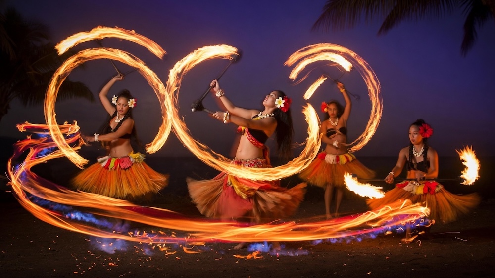 Female Ahi Lele fire dancers with the torches leaving trails as the dancers spin their fires working together