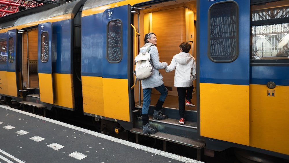 Mother and son holding hands, entering a blue and yellow public transport train